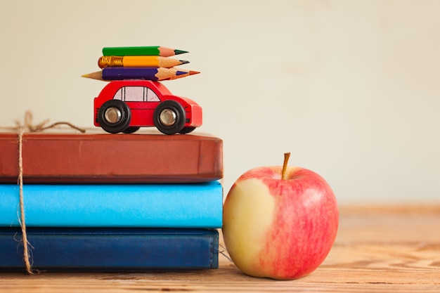 Torna al concetto di scuola con una pila di libri e mela rossa e auto in miniatura che trasportano matita colorata.
