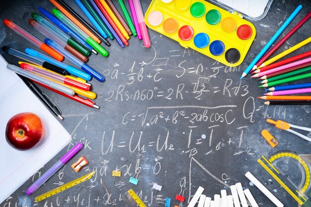 Torna al concetto di scuola, cornice con materiale scolastico colorato su sfondo lavagna con formule matematiche