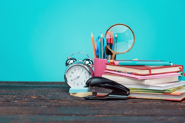 Torna al concetto di scuola. Libri, matite colorate e orologio sulla parete blu