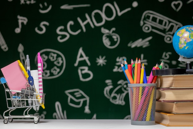 torna alla parete della scuola con libri, matite e globo sul tavolo bianco su sfondo verde.