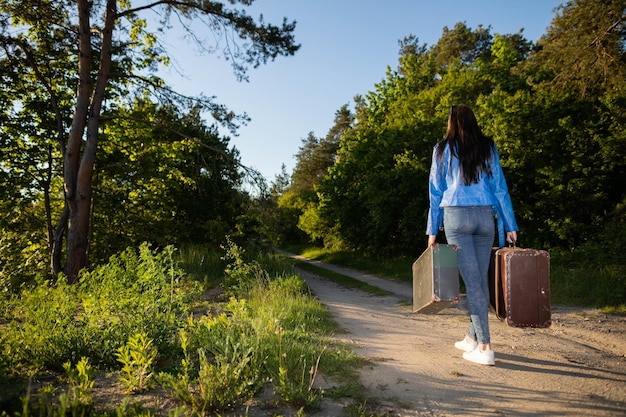 Tornare a casa in campagna dopo una vacanza di successo Camminare lungo la strada sabbiosa del paese con vecchie valigie pesanti tra gli alberi verdi