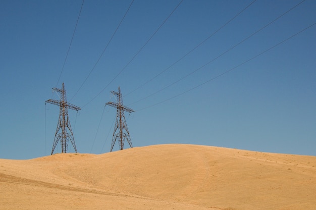 Torre ad alta tensione in una zona sabbiosa contro il cielo blu