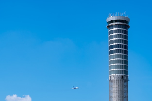 Torre di controllo del traffico aereo in aeroporto con volo aereo di volo internazionale sul cielo blu chiaro. Torre di controllo del traffico aeroportuale per il controllo dello spazio aereo tramite radar. Tecnologia aeronautica. Gestione del volo.