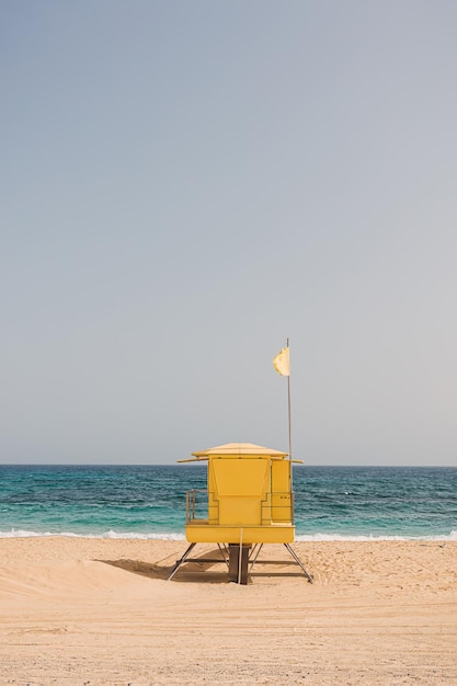 Torre di salvataggio in legno giallo sulla spiaggia di sabbia in una soleggiata giornata estiva durante il cielo del mare e lo sfondo della bandiera del nuoto Stazione bagnino Spazio di copia Concetto di vacanza