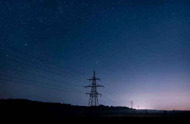 Torri di trasmissione di elettricità con fili luminosi contro il cielo stellato.