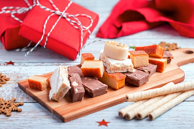 Torrone di dolci natalizi spagnoli tradizionali, polvorones, mantecados con decorazioni natalizie e scatole regalo rosse su tavolo in legno chiaro, spazio copia