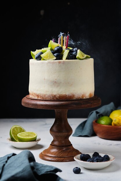 Torta agli agrumi su un supporto in legno, sul tavolo della cucina. Candele accese e fumo nella foto.