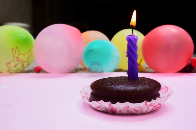 Torta al cioccolato con candela viola e Colorfull Baloon su sfondo rosa