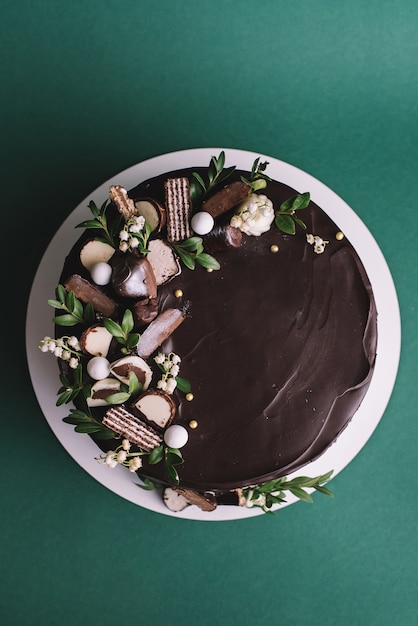 Torta al cioccolato con caramelle e fiori su sfondo verde, vista dall'alto