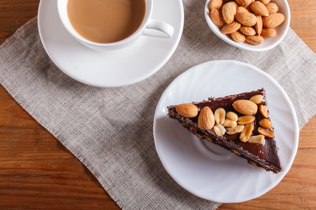 Torta al cioccolato con caramello, arachidi e mandorle su un fondo di legno marrone.