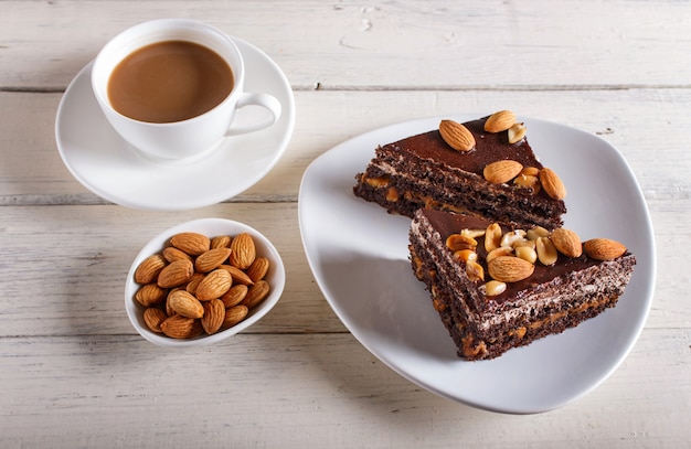 Torta al cioccolato con caramello, arachidi e mandorle su una superficie di legno bianca.