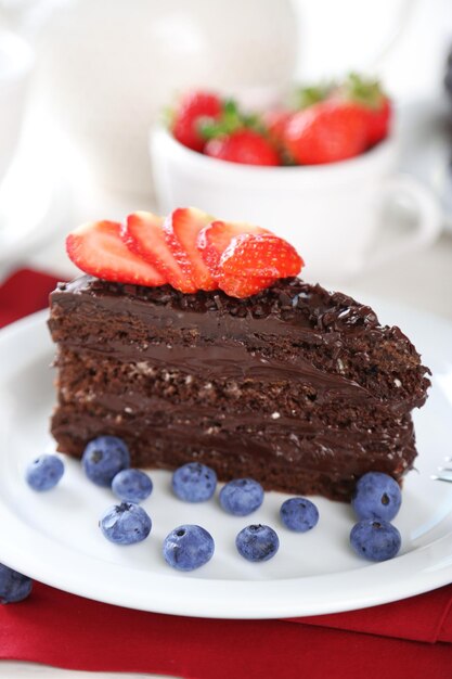 Torta al cioccolato con crema al cioccolato e frutti di bosco freschi sulla piastra sulla tavola di legno su sfondo chiaro