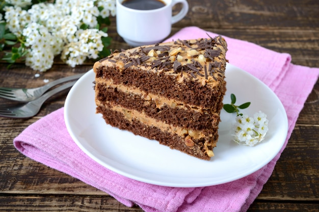 Torta al cioccolato con crema di noci su un tavolo di legno. Un pezzo di torta su un piatto e una tazza di caffè.