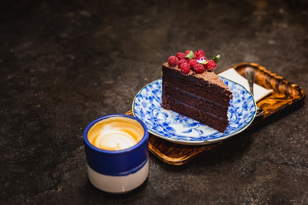 Torta al cioccolato con frutta lampone e tazza di caffè sul tavolo.