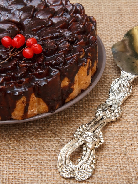 Torta al cioccolato decorata con grappolo di viburno e sollevatore di torta d'argento accanto sul tavolo con tela di sacco. Vista dall'alto.