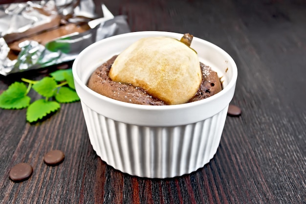 Torta al cioccolato e pera in una ciotola bianca, menta sullo sfondo di assi di legno scuro