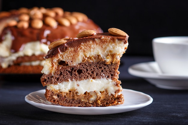 Torta al cioccolato fatta in casa con crema di latte, caramello e mandorle sul tavolo di legno nero.