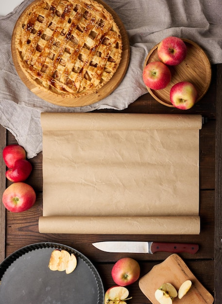 Torta al forno rotonda con ripieno di mele su una tavola di legno e tavolo marrone degli ingredienti