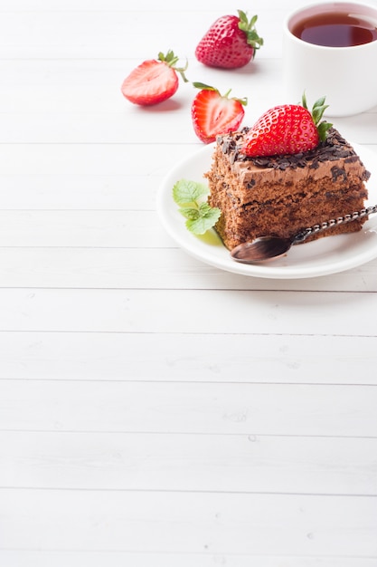 Torta al tartufo con cioccolato e fragole e menta su un tavolo di legno bianco.