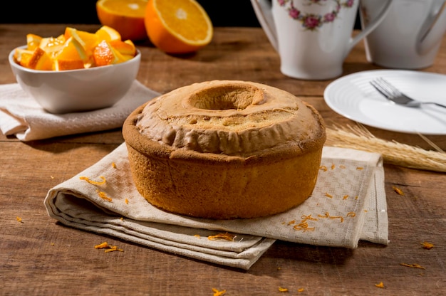 Torta all'arancia intera su legno con scorza d'arancia, pezzi d'arancia in barattolo bianco e torta sullo sfondo.