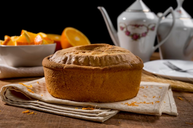 Torta all'arancia intera su legno con scorza d'arancia, pezzi d'arancia in barattolo bianco e torta sullo sfondo.