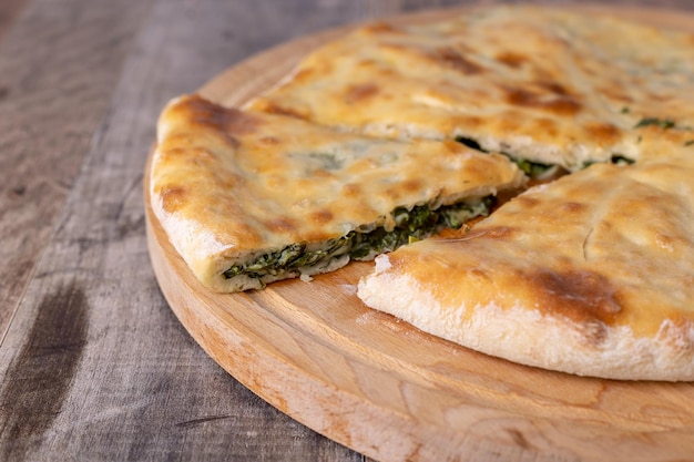 Torta alle erbe di spinaci e suluguni su una tavola di legno Torta intera con fetta tagliata