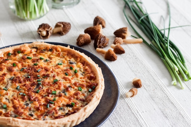 Torta aperta di quiche con funghi morel, cipolla e formaggio su un piatto