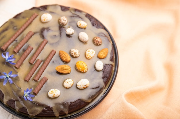 Torta brownie al cioccolato fatta in casa con crema al caramello e mandorle con una tazza di caffè su uno sfondo di cemento bianco e tessuto arancione. Vista laterale, primo piano, messa a fuoco selettiva.