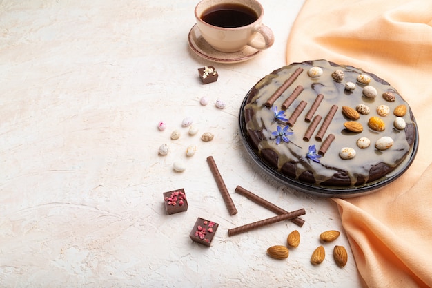 Torta brownie al cioccolato fatta in casa con crema al caramello e mandorle con una tazza di caffè su uno sfondo di cemento bianco.