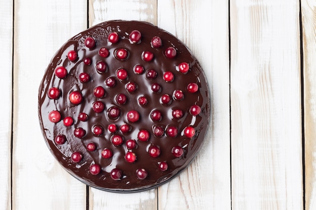 Torta brownie con glassa al cioccolato, decorata con mirtilli rossi, su fondo in legno chiaro. Senza glutine. Copia spazio