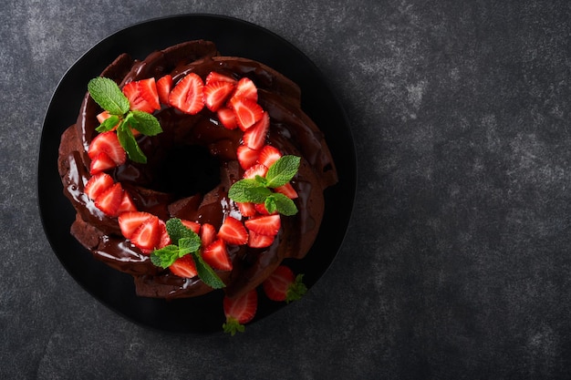 Torta Bundt al cioccolato fondente con glassa di Ganache e fragola su pietra scura o sfondo del tavolo in cemento Torta festiva Messa a fuoco selettiva