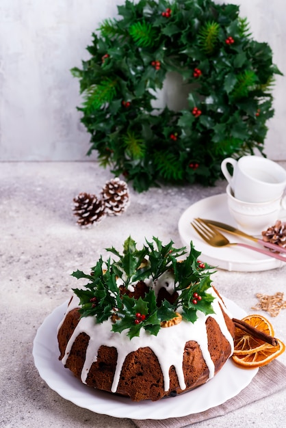 Torta bundt al cioccolato fondente di Natale decorata con glassa bianca e rami di bacche di agrifoglio su un cemento chiaro