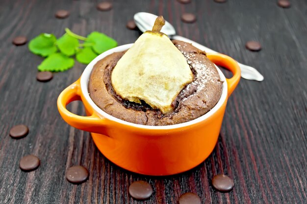 Torta con cioccolato e pera in torrefazione rossa, menta e cucchiaio su uno sfondo di assi di legno scuro