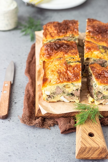 Torta con fegato, uova e aneto ripieno su una tavola di legno.