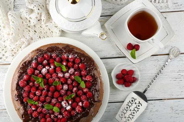 Torta con glassa al cioccolato e lamponi e tazza di tè su fondo di legno di colore