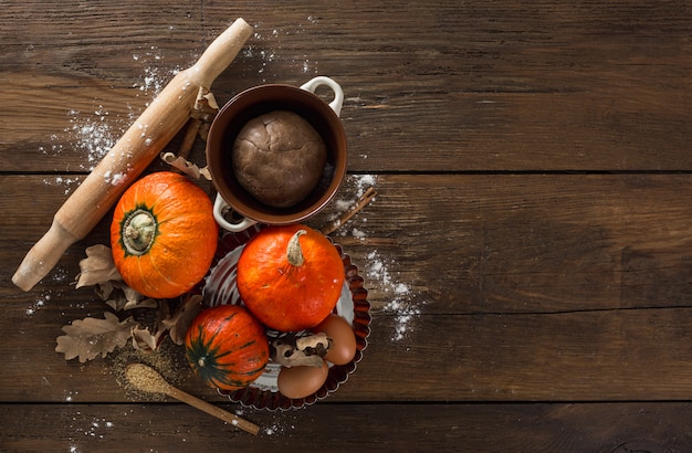 Torta cruda di torta di zucca con foglie secche autunnali, zucchero di canna, mattarello e bastoncini di cannella