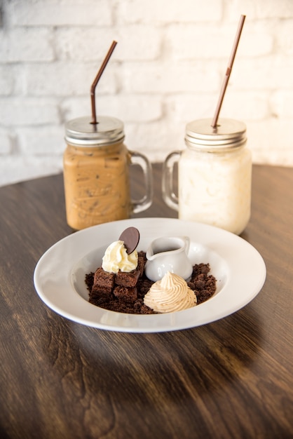 Torta del brownie con la priorità bassa della crema della frusta con la bevanda fredda caffè e frappè.