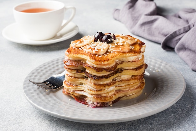 Torta del pancake con lo sciroppo della bacca e delle banane, fuoco selettivo, fondo grigio.