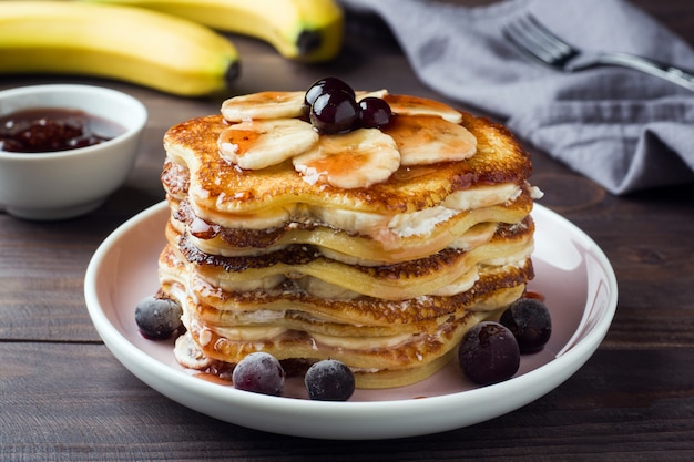 Torta del pancake con lo sciroppo della bacca e delle banane, fuoco selettivo, priorità bassa scura.