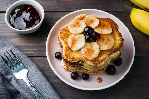 Torta del pancake con lo sciroppo della bacca e delle banane, fuoco selettivo, priorità bassa scura.