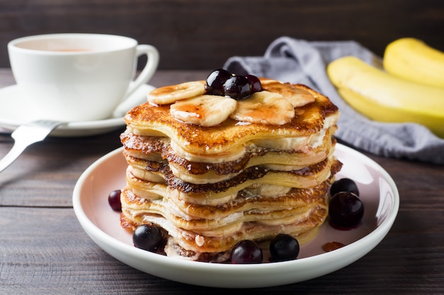 Torta del pancake con lo sciroppo della bacca e delle banane, fuoco selettivo, priorità bassa scura.