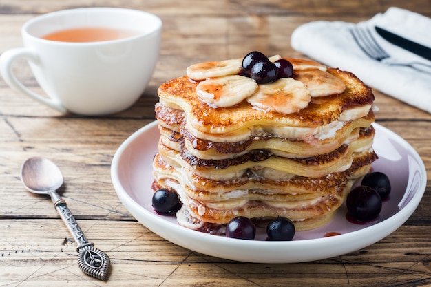 Torta del pancake con lo sciroppo della bacca e delle banane, fuoco selettivo, priorità bassa scura.