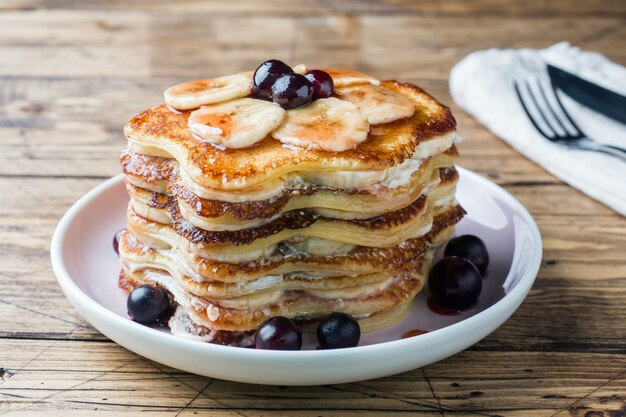 Torta del pancake con lo sciroppo della bacca e delle banane, fuoco selettivo, priorità bassa scura.