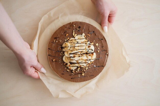 Torta di banana al cioccolato fatta in casa con le mani su carta pergamena Consegna del cibo Cottura fatta in casa Vista dall'alto Deliziosa crostata con cioccolato e banana sul tavolo di legno