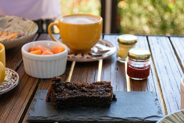 Torta di biscotti su una tavola di ardesia, accanto a marmellate assortite, papaya e tazza di latte.