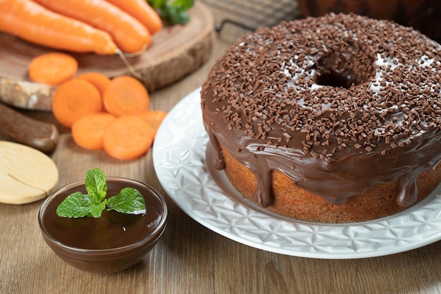 Torta di carote brasiliana con glassa di cioccolato su tavola di legno con carote in background