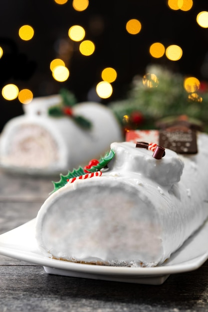 Torta di ceppo di Natale al cioccolato bianco con luci di Natale sul tavolo di legno