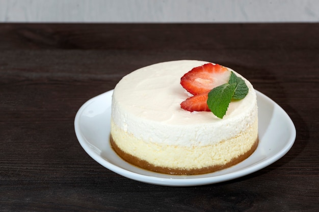 Torta di cheesecake delicata con fragole fresche e menta sulla zolla bianca su fondo di legno