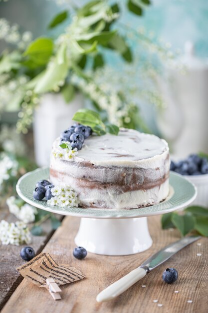 Torta di ciliegie fatta in casa con crema al mascarpone su uno sfondo chiaro e un bouquet di fiori di ciliegio e lillà.