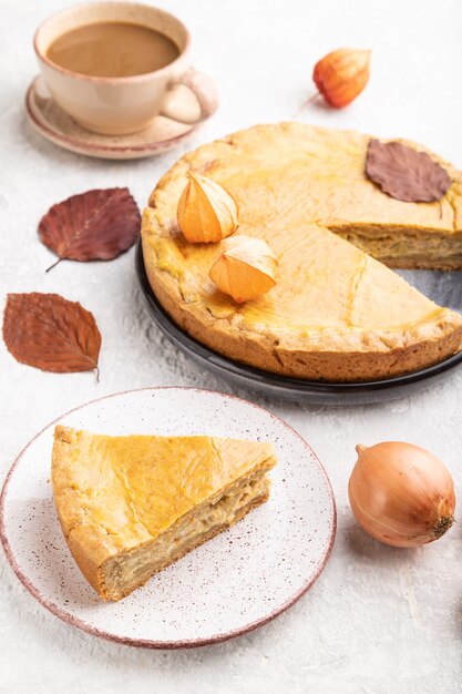 Torta di cipolle autunnale decorata con foglie e tazza di caffè su cemento grigio